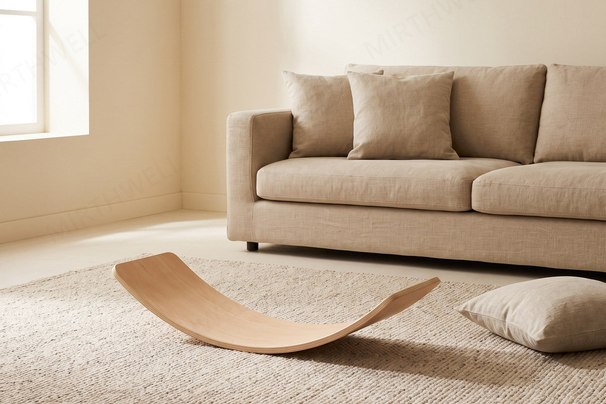A curved wooden balance board lying on an oatmeal wool rug in a cream-walled living room, with the edge of a linen sofa and its cushions visible behind it and daylight coming from a window on the left.