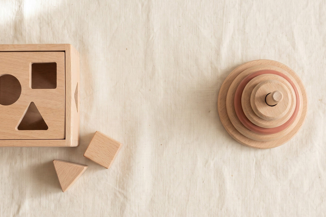 A wooden shape-sorter and a wooden ring-stacker side by side on cream linen