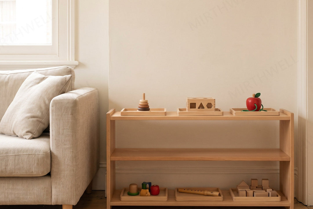 A low two-tier wooden shelf against a living room wall beside the corner of a sofa, holding five wooden toys on plain trays with space between them, a small woven mat on the floor in front.