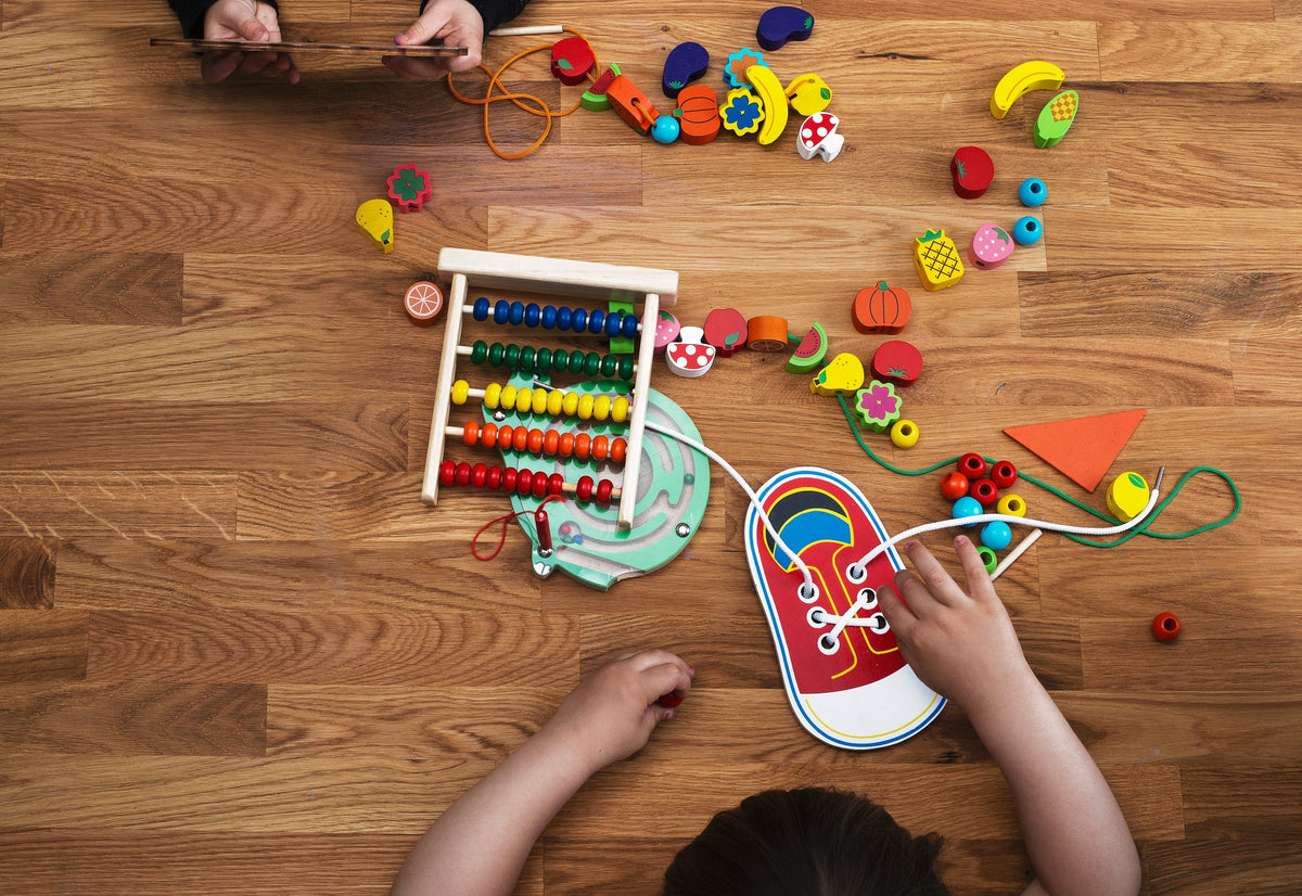 Wooden toys seen from above on a wooden floor, with two children playing