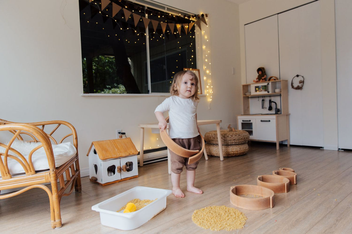 A toddler playing on the floor with a few wooden toys in a calm, uncluttered room