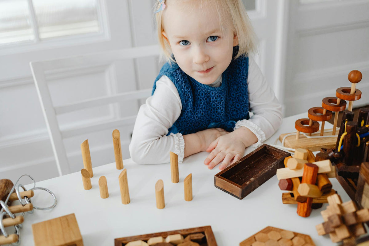 A child at a home table with wooden pegs and blocks laid out in front of her