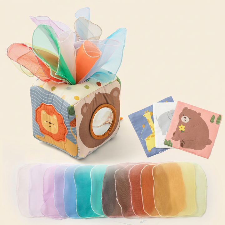 Soft fabric Montessori magic tissue box cube on warm cream - bear-face mirror panel with rainbow crinkle scarves and printed animal cloths