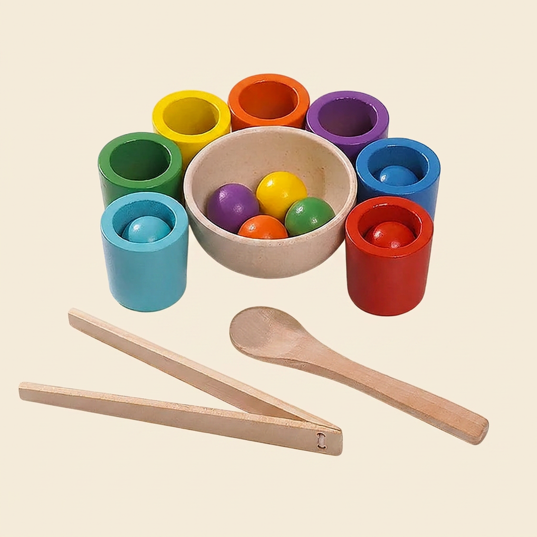 Wooden color-sorting cups set on warm cream - seven rainbow cups, matching wooden balls, a bowl, spoon and tongs
