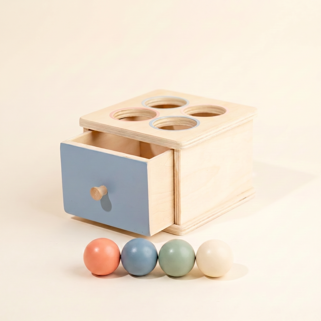 Wooden Montessori drawer box on warm cream - ball-drop box with pastel blue drawer and four wooden balls