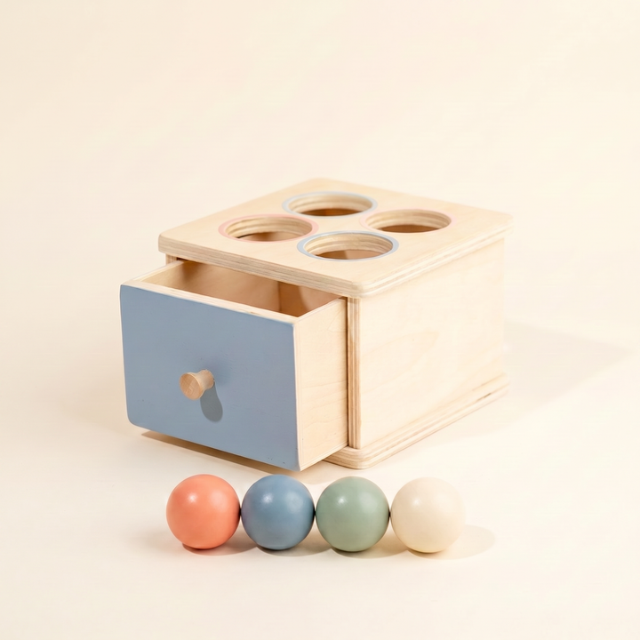 Wooden Montessori drawer box on warm cream - ball-drop box with pastel blue drawer and four wooden balls