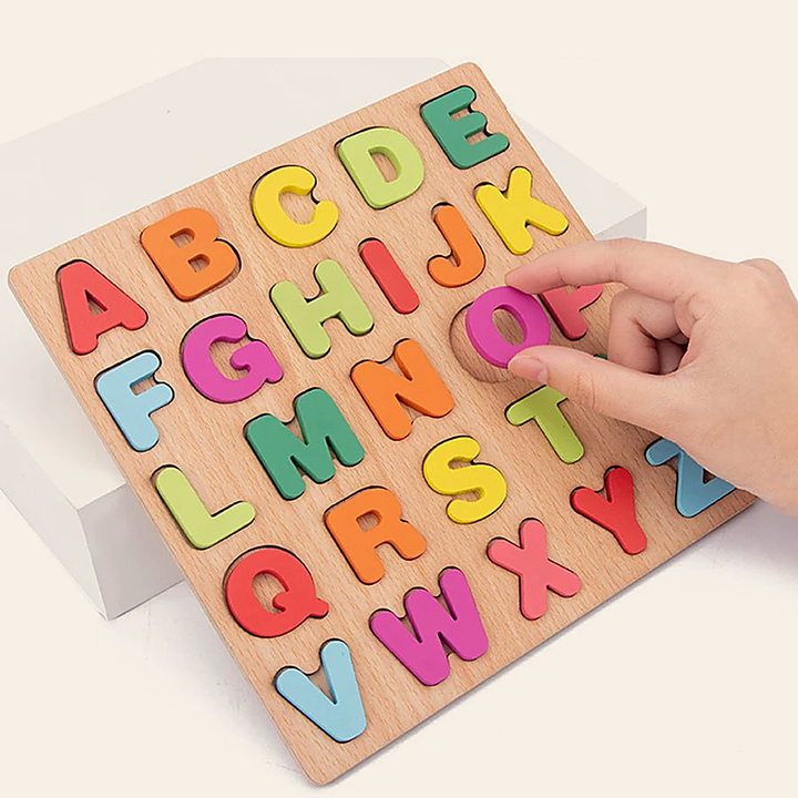 A hand placing a chunky wooden letter into its matching slot on the capital-letters board