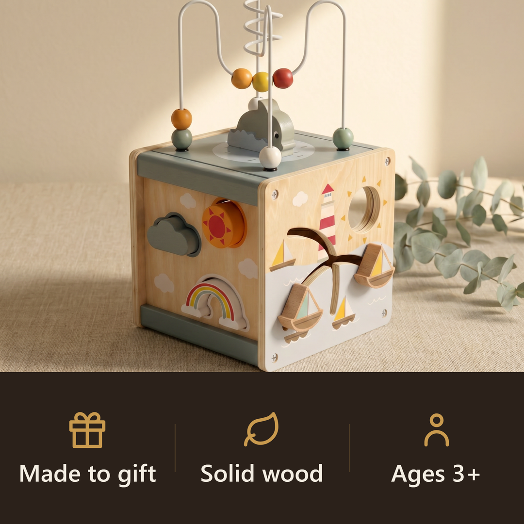 The wooden 5-in-1 activity cube on linen with eucalyptus. Badges: made to gift, solid wood, ages 3+.
