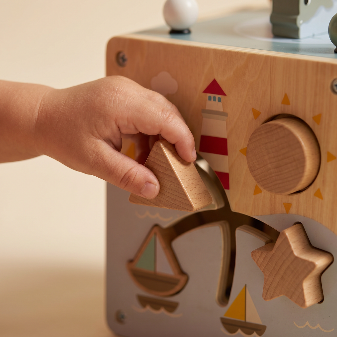 Close-up of a toddler's hand posting a wooden shape into the shape-sorter side of the activity cube.