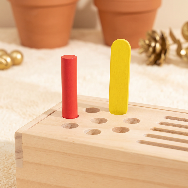 Close-up of the slotted wooden lid with a rainbow peg and flat stick in their matching slots