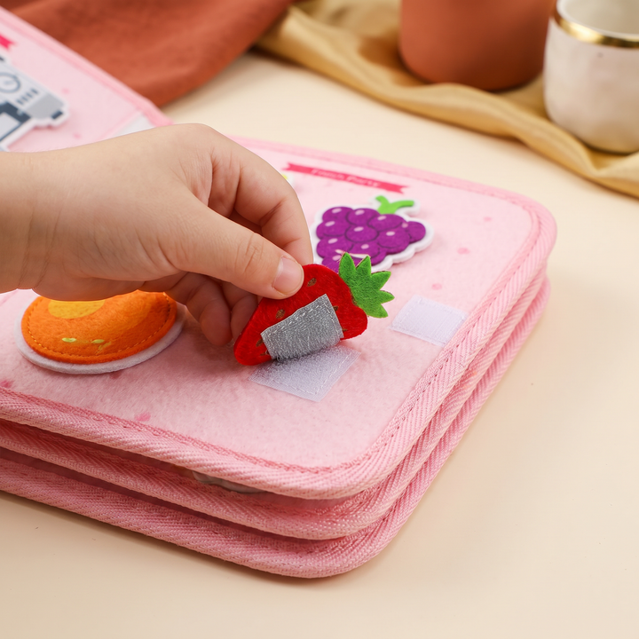 Close-up of small fingers peeling a felt strawberry piece off a cloth page