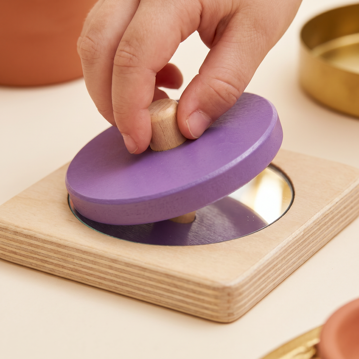 Close-up of small fingers lifting the purple knob disc to reveal the round mirror