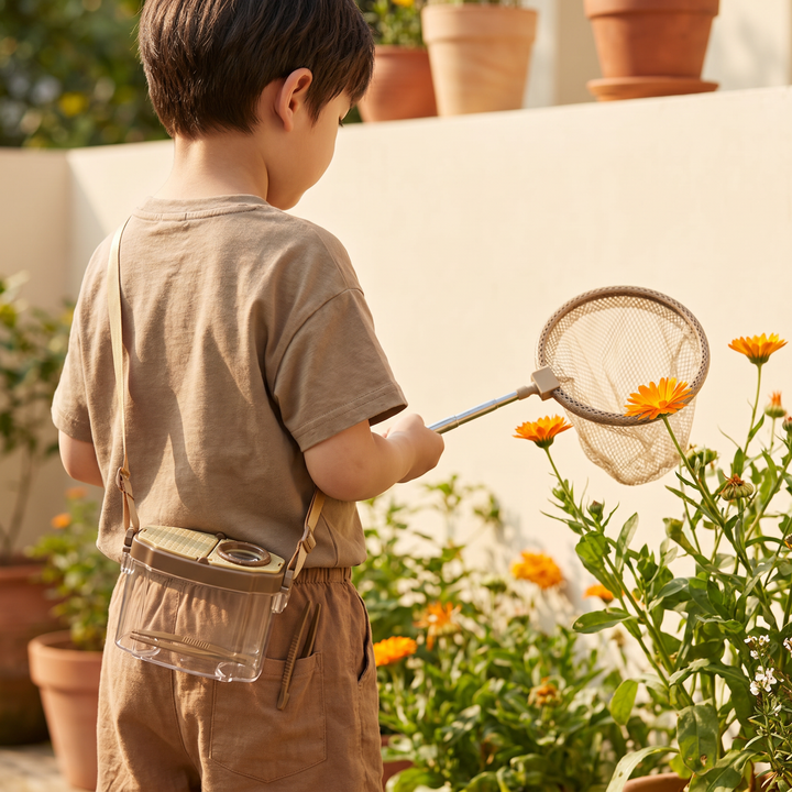 A young child outdoors with the bug net over one shoulder, scooping toward a flower