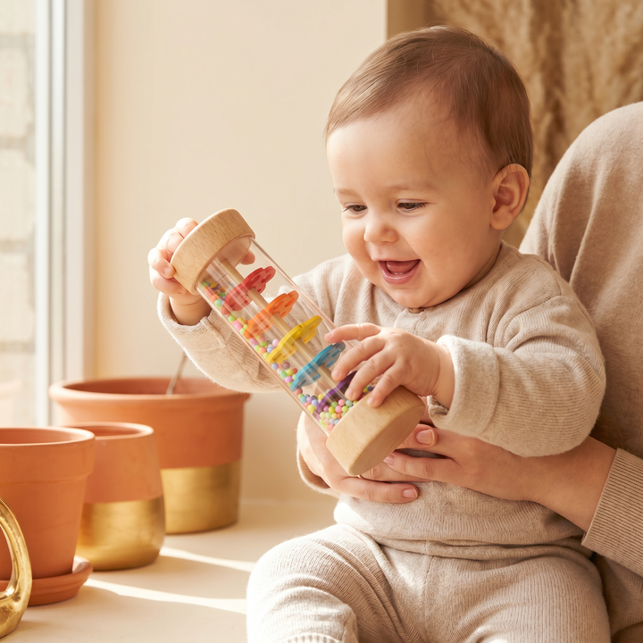A baby tipping the small wooden rainmaker to watch the colorful beads fall